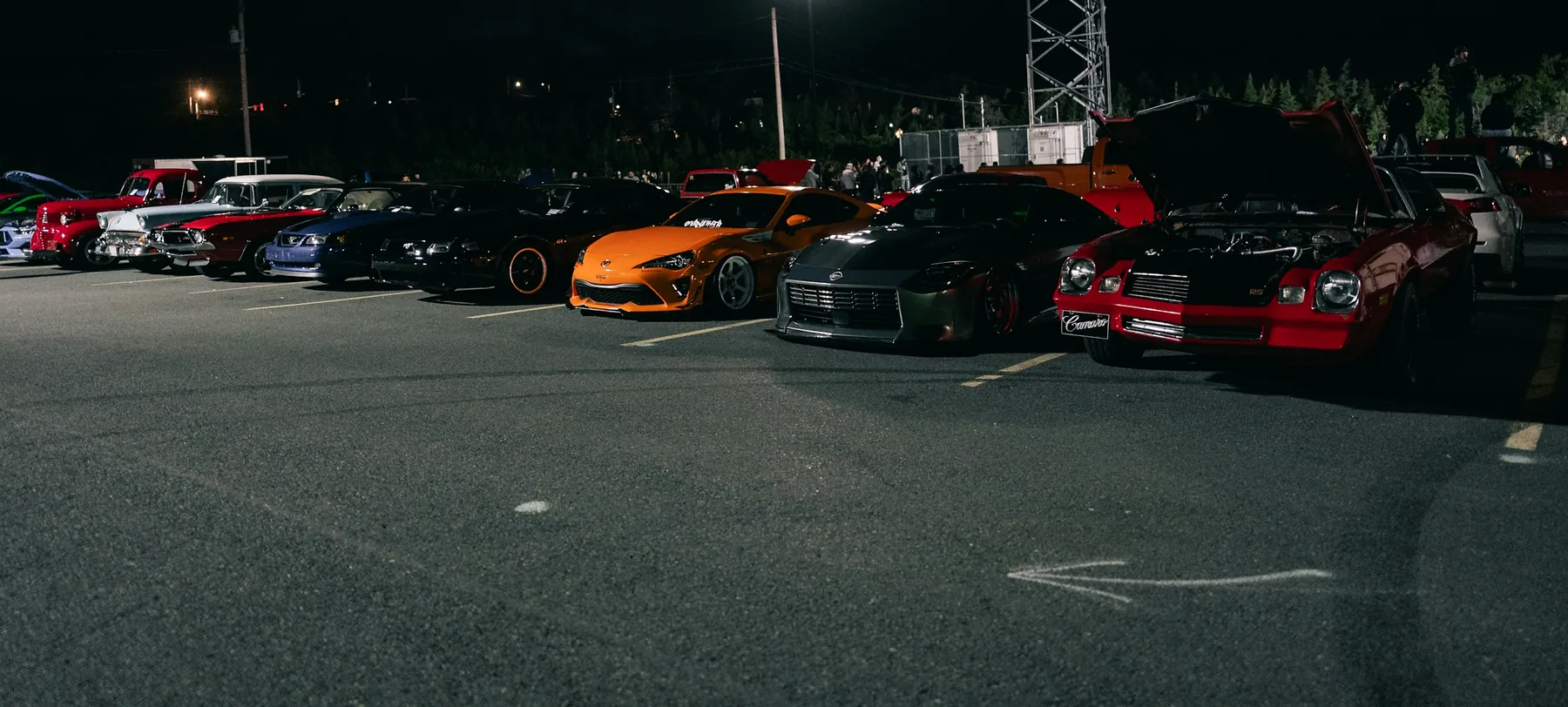 A night meet in a car park: a row of modified cars under floodlights